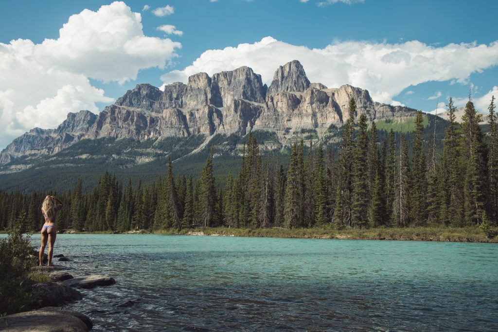 Woman in bikini standing by the lake and looking at mountains and forest